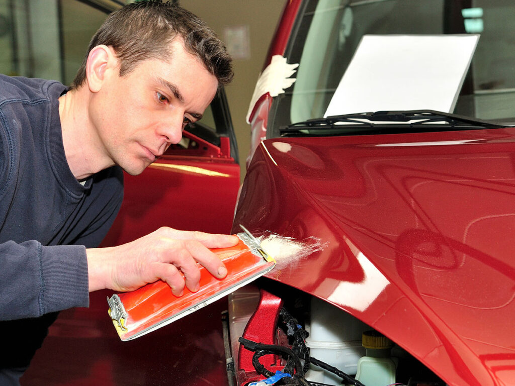 man repairing damage to red car