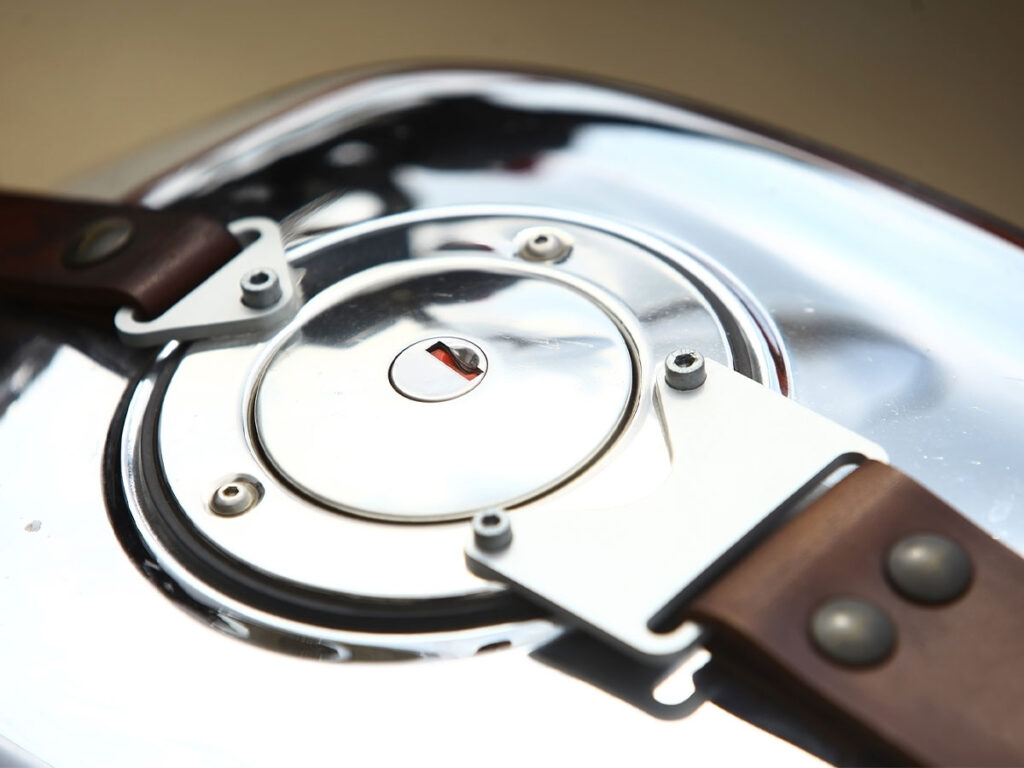 Closeup of a chrome motorcycle gas tank with leather straps.